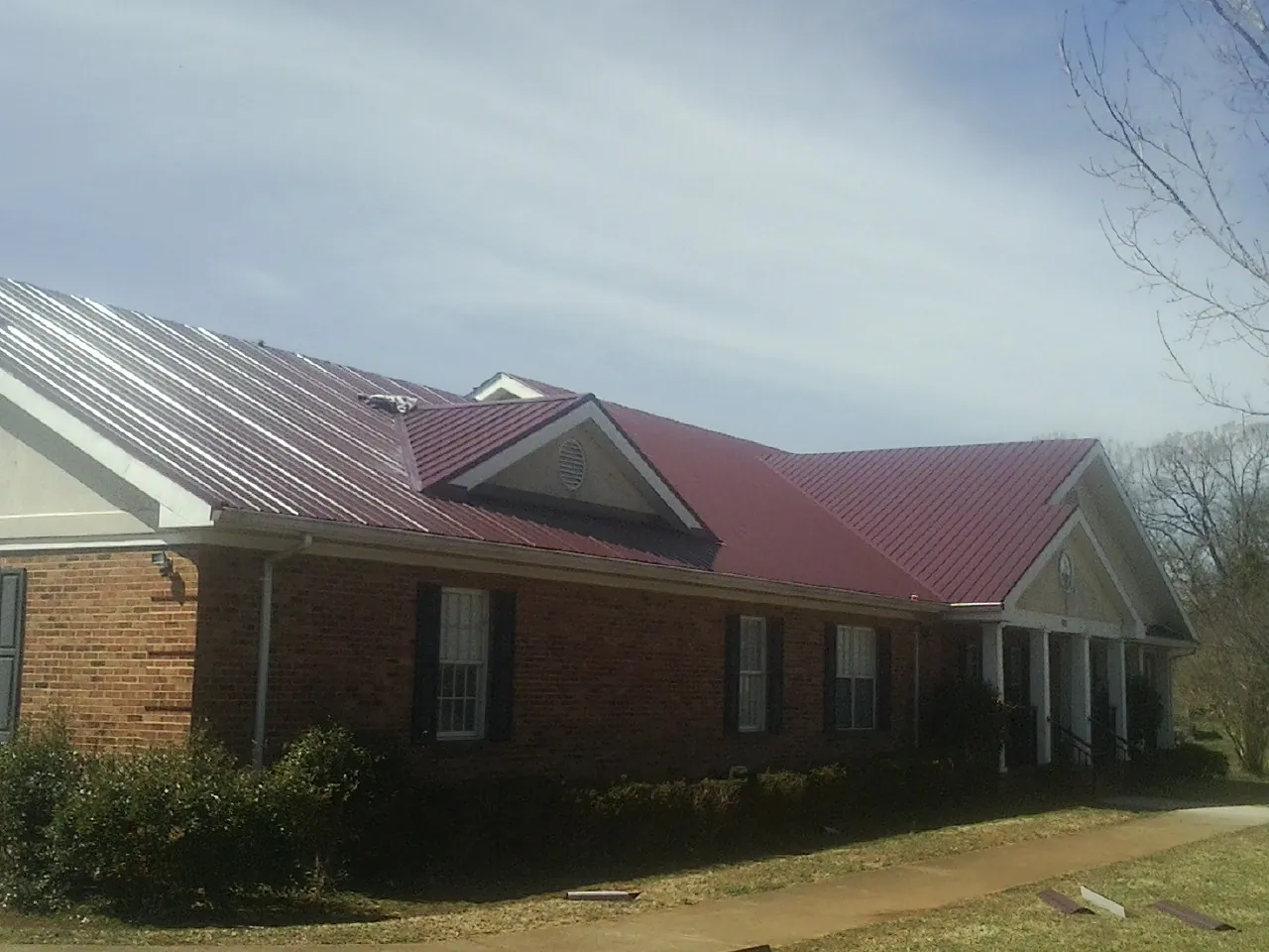 Red metal roof with gabled entries on a long brick building, from a Hail Damage Roof Repair job in Beech Creek