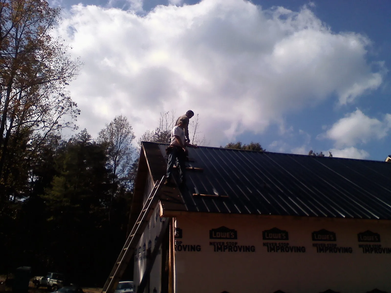 Roofer fastening dark metal panels high against a cloudy sky, from a Roof Inspection job in Beech Creek