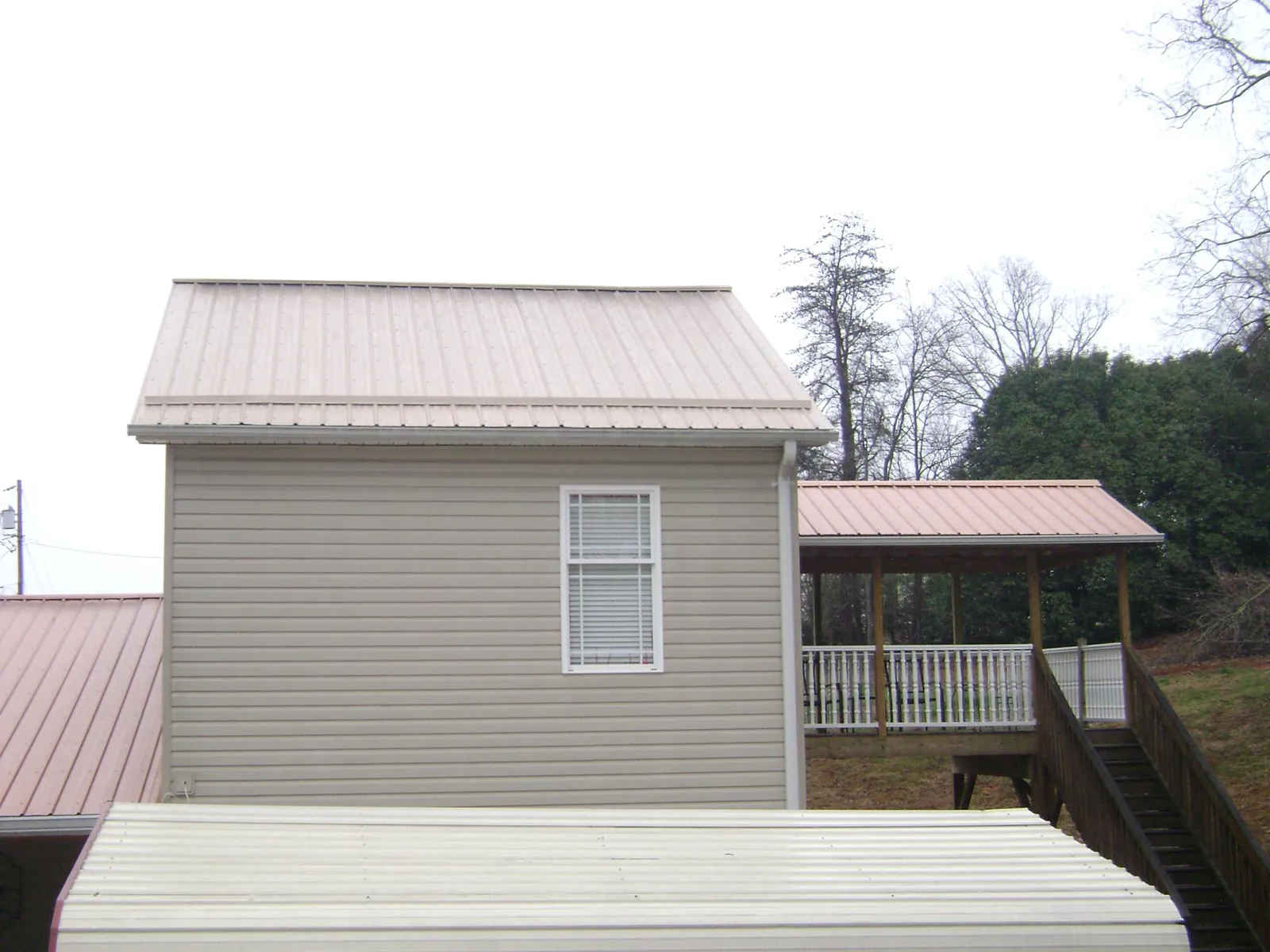 Tan metal roofs on a two story addition and attached porch, from a Roof Replacement job in Beech Creek